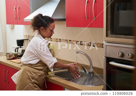 Woman washing hands at kitchen sink with red cabinets 119806026
