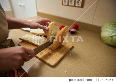 Person slicing fresh bread on a wooden cutting board in kitchen Person slicing fresh bread on a wooden cutting board in kitchen 119806063