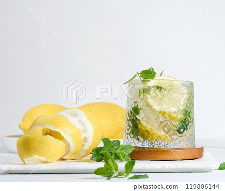 Transparent glass with lemon slices, mint leaves and ice cubes on white table Transparent glass with lemon slices, mint leaves and ice cubes on white table 119806144