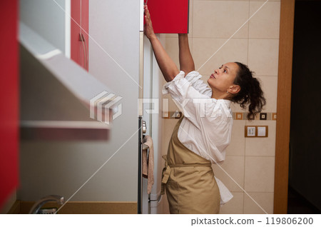 Woman reaching up to a kitchen cabinet in a modern home 119806200