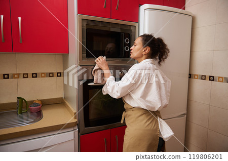 Woman cleaning oven in modern kitchen with red cabinets 119806201