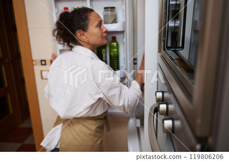 Woman looking inside refrigerator in bright modern kitchen Woman looking inside refrigerator in bright modern kitchen 119806206