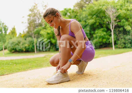 An Active Woman is Skillfully Tying Her Shoelaces While Enjoying the Park Environment 119806416
