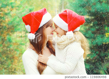 Christmas family child hugging mother in santa red hats together over a tree Christmas family child hugging mother in santa red hats together over a tree 119806498