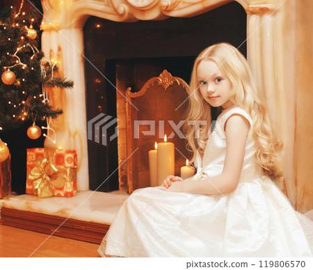 Child little girl in dress near christmas tree and fireplace at home Child little girl in dress near christmas tree and fireplace at home 119806570