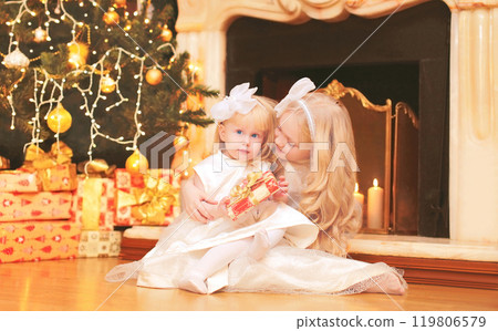 children little girls with gift boxes near christmas tree and fireplace at home 119806579