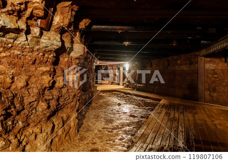 Exploring the Long Dark Wet Mine Tunnel with Wooden Walkway and Rough-Cut Stone Walls Illuminated, gold mine 119807106