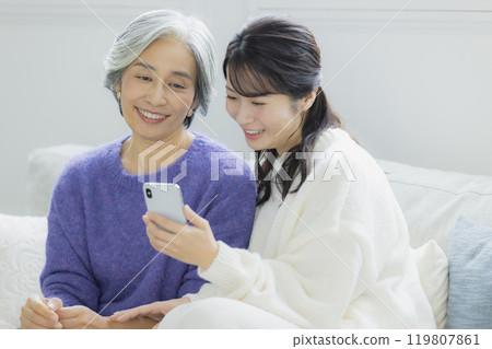 Senior woman and young woman looking at smartphones in the living room Senior woman and young woman looking at smartphones in the living room 119807861