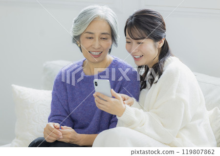 Senior woman and young woman looking at smartphones in the living room 119807862