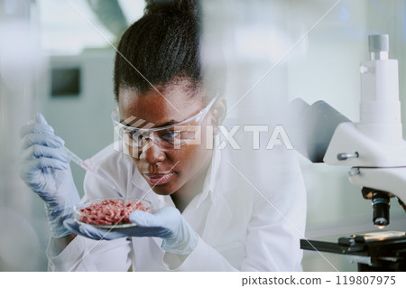 Scientist wearing protective gear analyzing tissue samples under microscope in laboratory environment with concentration and precision 119807975