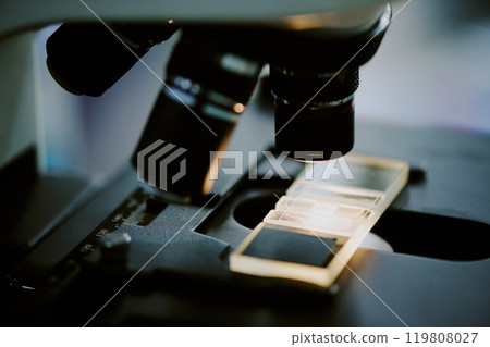 Microscope slide placed under the lenses of a laboratory microscope showing detailed components and parts. Image captures intricate details within a scientific research setting 119808027