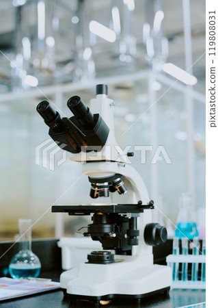 Close-up of advanced microscope in a high-tech laboratory environment featuring equipment and glass containers in the background 119808031