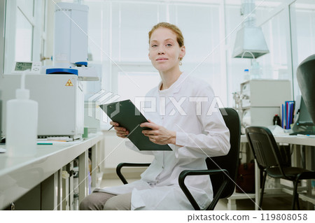 Portrait of scientist in a laboratory holding clipboard and analyzing data surrounded by scientific equipment, with bright windows providing ambient light Portrait of scientist in a laboratory holding clipboard and analyzing data surrounded by scientific equipment, with bright windows providing ambient light 119808058