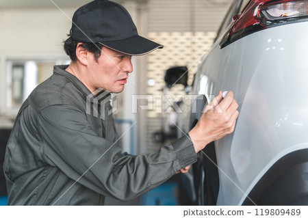 一名男性機械師正在用觸摸筆擦拭汽車保險桿(去除刮痕、修補油漆、修補) 一名男性機械師正在用觸摸筆擦拭汽車保險桿(去除刮痕、修補油漆、修補) 119809489
