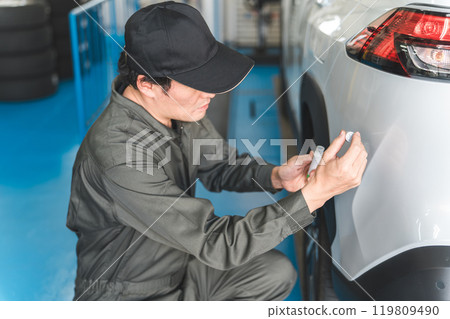 A male mechanic applying a touch pen to a car bumper (removing scratches, repairing paint, touching up) A male mechanic applying a touch pen to a car bumper (removing scratches, repairing paint, touching up) 119809490