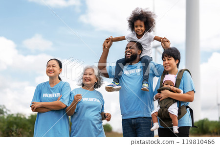 family of volunteers are standing together, with a baby being carried by a man 119810466