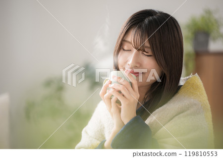 Close-up of a relaxing young woman drinking a hot drink in her living room in winter Close-up of a relaxing young woman drinking a hot drink in her living room in winter 119810553