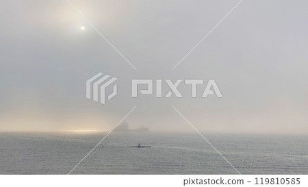 Man in a boat sailing on the sea in the fog on the background of the ship Man in a boat sailing on the sea in the fog on the background of the ship 119810585