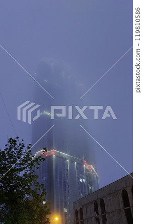 A high-rise building disappears in the evening fog 119810586