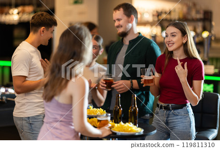 Happy mens and womens drinking beer and eating crisps, laughing and spending time together in bar Happy mens and womens drinking beer and eating crisps, laughing and spending time together in bar 119811310