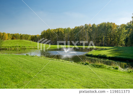A serene and tranquil pond featuring a beautiful fountain amidst a lush green landscape A serene and tranquil pond featuring a beautiful fountain amidst a lush green landscape 119811373