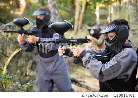 Paintball players aiming and shooting with guns at opposing team 119811401