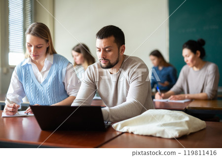 Group of adult students sitting at tables in classroom Group of adult students sitting at tables in classroom 119811416