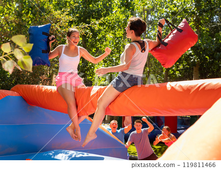 Happy girl funny pillow fighting on inflatable log with female friend 119811466
