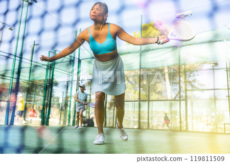 Athletic woman plays padel outdoor. View through tennis net 119811509