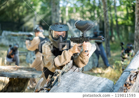 Paintball player in protective uniform aiming and shooting with guns Paintball player in protective uniform aiming and shooting with guns 119811593