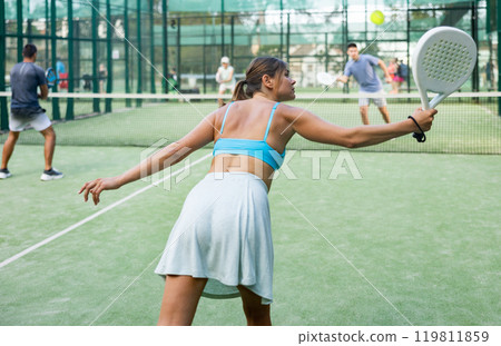 Rear view of young woman playing padel on open court 119811859