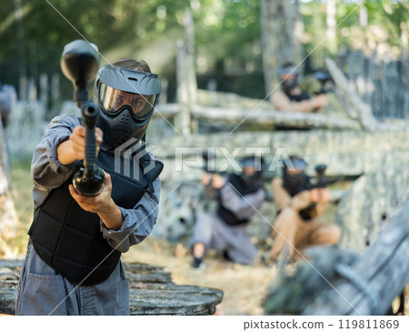 Paintball player in protective uniform aiming and shooting with guns Paintball player in protective uniform aiming and shooting with guns 119811869