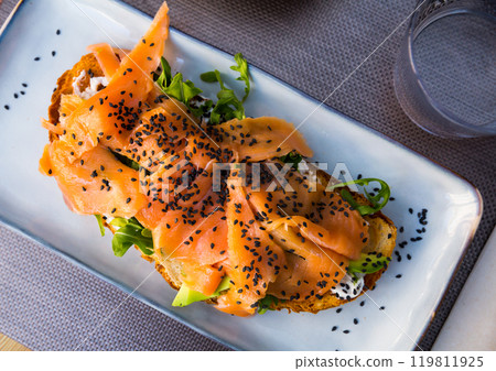 Delicious smoked salmon with arugula avocado and seeds on fried bread 119811925