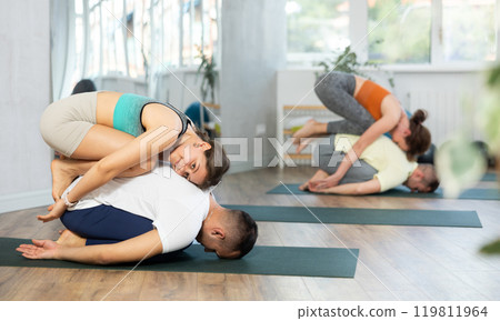 Young married couple meditate together in various yoga poses during group training in gym 119811964