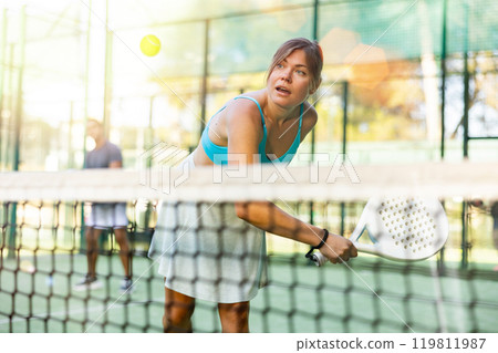 Young woman hitting ball with backhand during paddleball match outdoor 119811987