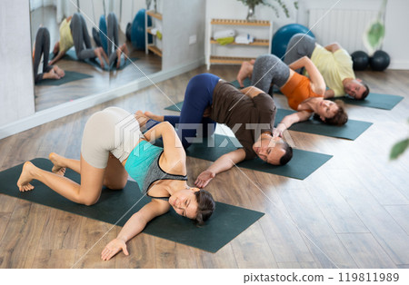 Group of people doing yoga with group in studio, performing hamstring and low back stretching Ardha Pawanmuktasana 119811989