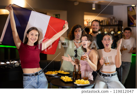 Happy girl with French flag celebrates the victory of her favorite team with a group of friends in beer bar 119812047