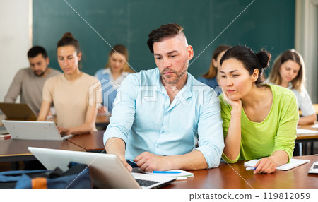 Two students studying is on a laptop, discussing something Two students studying is on a laptop, discussing something 119812059