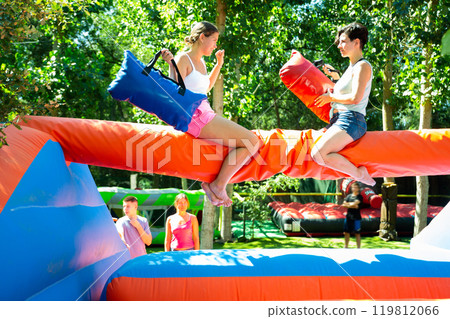 Laughing young girl fighting by pillows with female opponent on inflatable beam Laughing young girl fighting by pillows with female opponent on inflatable beam 119812066