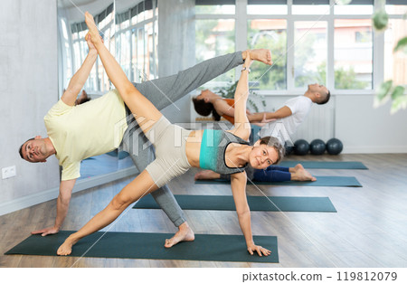 Lovers of active lifestyle perform pair yoga double side plank in gym Lovers of active lifestyle perform pair yoga double side plank in gym 119812079