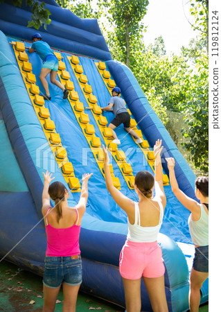 Two male friends climbing on inflatable slide with wooden poles Two male friends climbing on inflatable slide with wooden poles 119812124