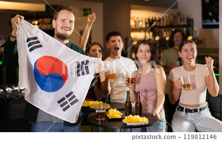 Football fans gesturing emotionally after goal scored by favorite team while watching championship match on TV in sports bar with North Korea flag Football fans gesturing emotionally after goal scored by favorite team while watching championship match on TV in sports bar with North Korea flag 119812146
