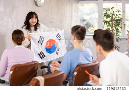 Young woman teacher holding flag of South Korea in front of group of students 119812283