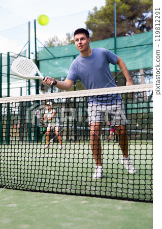 Young guy playing padel tennis on open court in summer Young guy playing padel tennis on open court in summer 119812291