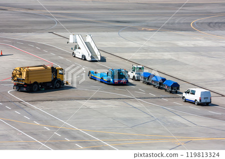 Airfield universal cleaning machine, pushback tug, passenger boarding steps vehicle, tractor with baggage carts and minivan at the airport 119813324