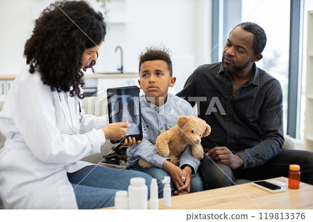 Female doctor shows lung x-ray to sick boy with father at home 119813376
