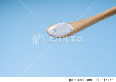 White baking soda powder lifted from a wooden spoon on a light blue background White baking soda powder lifted from a wooden spoon on a light blue background 119813432