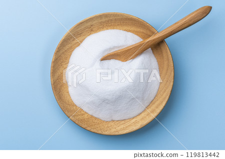 An overhead view of white baking soda powder with a wooden bowl and wooden spoon on a blue background 119813442