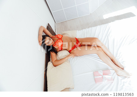 Beautiful woman in red lingerie on white bed in bedroom in morning 119813563