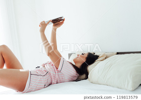 brunette woman in pajamas in bedroom talking on internet smartphone brunette woman in pajamas in bedroom talking on internet smartphone 119813579